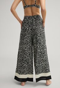 Spodnie szerokie w nogawkach z czarno-białym abstrakcyjnym wzorem, wykonane z lekkiego materiału, z kontrastującymi czarnymi i kremowymi detalami na dolnej krawędzi.