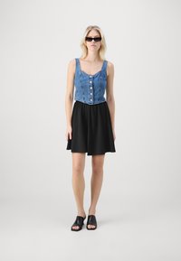 Farmerdzsebb crop top gombokkal, fekete harangszoknyával és nyitott orrú fekete cipővel párosítva. A modellen sima fekete napszemüveg van.