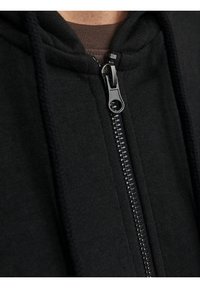 Černá mikina na zip s texturovanou látkou, opatřená kovovým zipem a šňůrkami. Detailní pohled zdůrazňuje švy a detaily zipu.