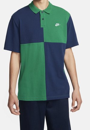 Uomo che indossa una polo Nike a maniche corte con blocchi di colore verde e blu navy e un logo Nike bianco sul petto.