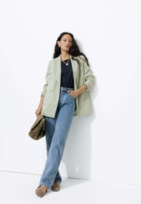 Blazer double boutonnage vert clair, chemise bleu marine, jean taille haute bleu, ballerines imprimé léopard et un sac à main vert avec un accent chaîne.