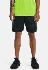 Zwarte sportieve shorts van een gladde stof met een relaxte pasvorm, gecombineerd met een felgroen shirt en zwarte schoenen.