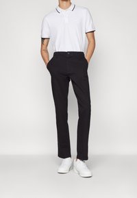 Vit polo skjorta med svart krage, i kombination med mörka byxor och vita sneakers. Outfiten är enkel och avslappnad i designen.