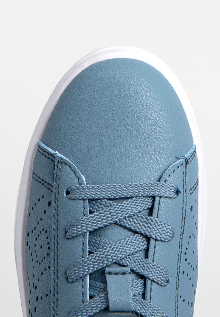Zapatilla de cuero azul con diseño perforado, cordones planos y suela de goma blanca. Presenta una textura lisa y una forma de punta redonda.