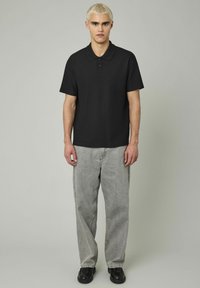 Chemise polo noire à manches courtes avec une finition texturée, associée à un jean large gris clair et des chaussures noires. Design simple et moderne.