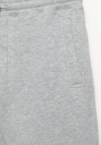 Light gray sweatpants close-up showing front pocket, elastic waistband with drawstring, and soft cotton fabric texture.