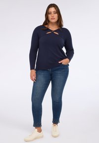 Maglione blu navy con un design a coste, dotato di due aperture frontali e maniche lunghe. Abbinato a jeans skinny arricchiti da borchie.