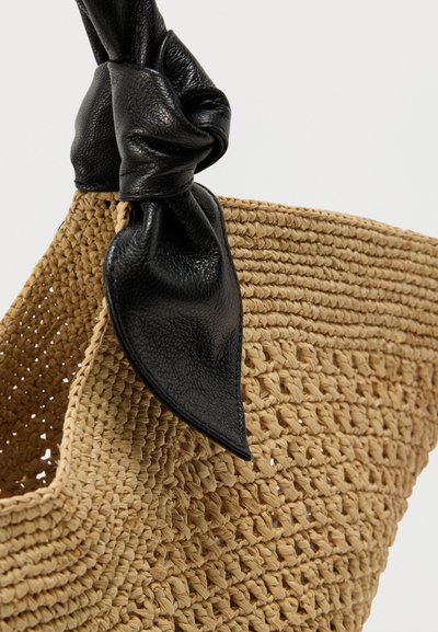 Πλεκτή τσάντα ώμου από ψάθα σε φυσικό μπεζ χρώμα, με μαύρο δερμάτινο κόμβο ως διακοσμητικό στο πάνω μέρος. Υφή με ανάγλυφη επιφάνεια, ανοιχτού τύπου σχεδίαση.