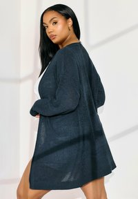 Marinblå stickad kofta med långa ärmar, öppen framsida, ribbat nederkant och textil material, med sidofickor för extra komfort.