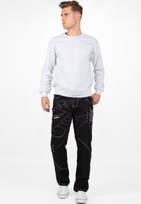 Felpa grigia, jeans neri con cuciture bianche e molteplici tasche, indossati con sneakers bianche. Outfit semplice e casual.