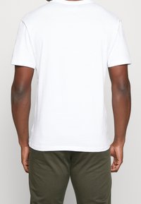 Vit bomull t-shirt, korta ärmar, rund hals, avslappnad passform, slät textur, inga synliga mönster eller logotyper. Bakre vy visad.