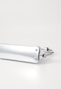 Zilveren metallic handtas met een gladde textuur, smalle rechthoekige vorm en een gebogen handvat. Voorzien van zilveren hardware en stiksels als accent.