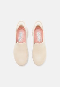 Beżowe buty wsuwane z teksturowaną siateczkową powierzchnią, zaokrąglonym noskiem i wyściółką z amortyzacją z różowymi akcentami oraz brandingiem wewnątrz.