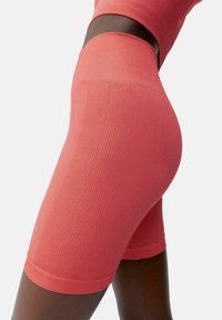 Korta leggings i en ljus korallfärg, med en ribbad struktur, elastisk midja och en figurnära design som följer kroppens konturer.