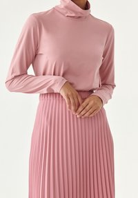 Halenka s dlouhým rukávem a rolákem ve světlé růžové barvě. Plisovaná sukně ve stejné růžové s elastickým pasem. Strukturovaný, hladký povrch.