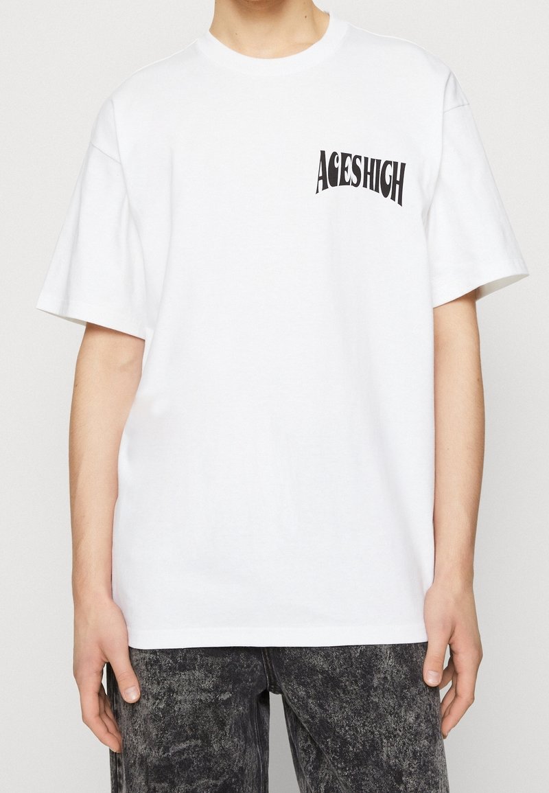 Biała bawełniana koszulka z czarnym, zakrzywionym nadrukiem "ACESHIGH" na lewej piersi. Krótkie rękawy, okrągły dekolt, luźny krój.