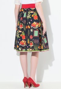 Blumenmusterrock mit schwarzem Hintergrund, rotem Bund und weißen Akzenten. Ein Paar rote Wildlederschuhe mit hohen Absätzen vervollständigt den Look.
