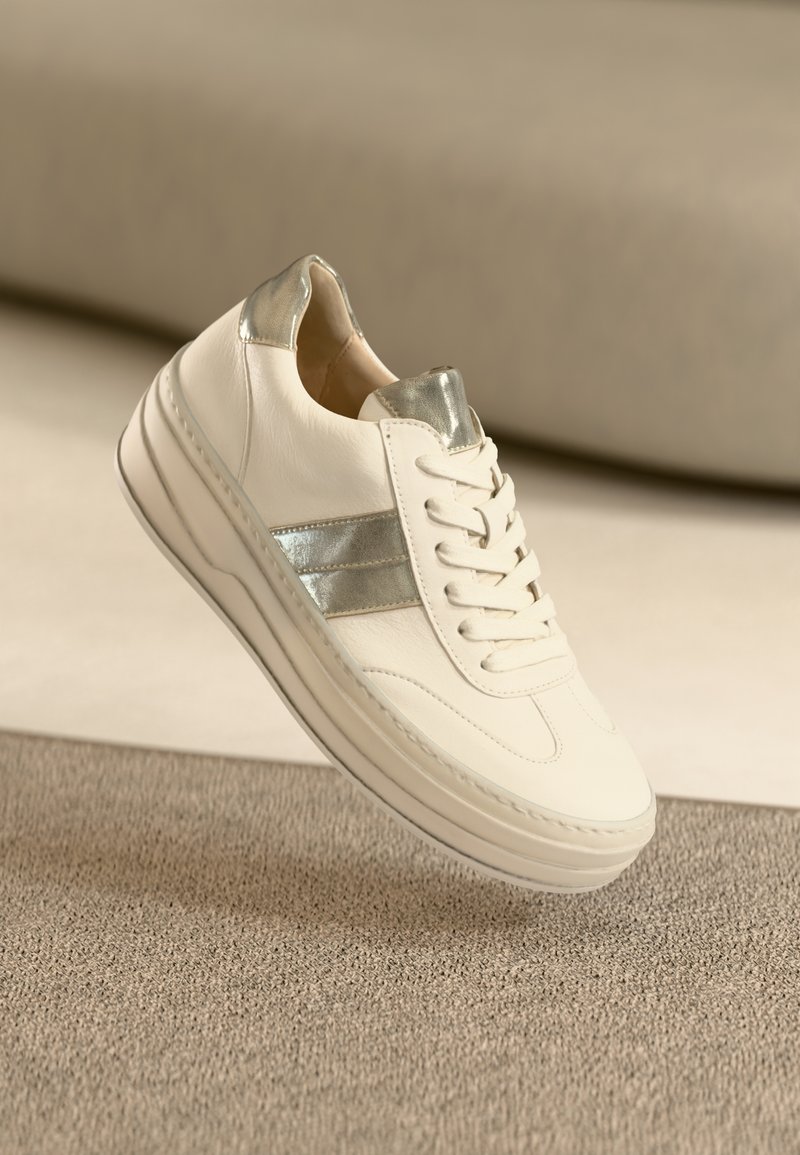 White leather sneaker with metallic silver accents, round toe, lace-up closure, and textured rubber sole. Minimalist design with smooth finish.