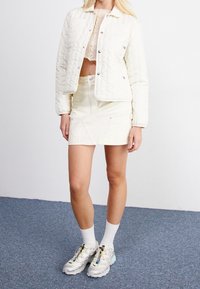 Vaalea tikattu takki, kerma crop-top, luonnonvalkoinen minihame ja hopeiset lenkkarit pastellisävyillä. Pintahaihtuva kangas ja tyylikäs muotoilu.