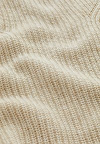 Tissu tricoté couleur crème avec un motif côtelé doux et texturé et de légers plis.