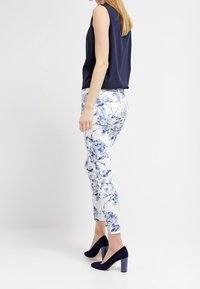 Blusa sin mangas azul marino combinada con pantalones ajustados blancos con estampado floral. La modelo lleva zapatos de tacón alto de ante azul marino. Las telas son suaves y ajustadas.