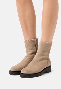 Botas de tobillo de ante beige con suela texturizada, cierre de cremallera y forro suave en el borde superior. Diseño elegante con acentos mínimos.