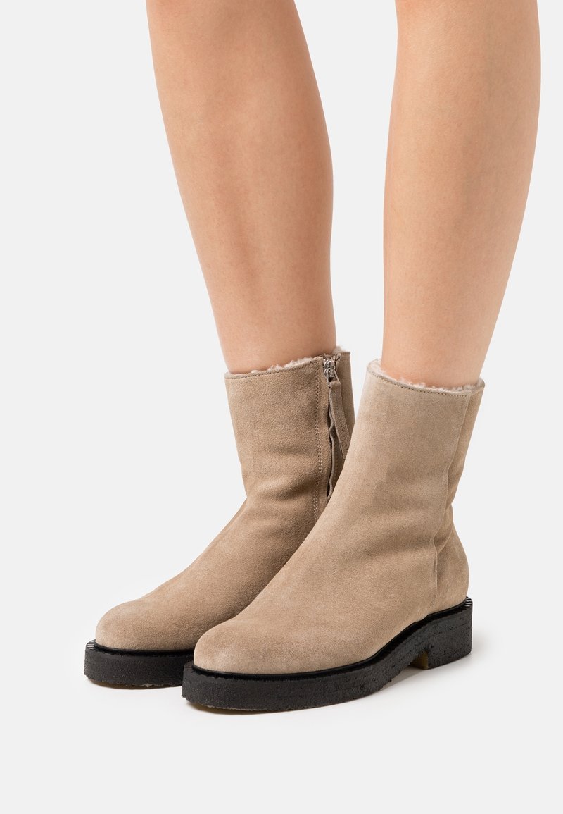Botas de tobillo de ante beige con suela texturizada, cierre de cremallera y forro suave en el borde superior. Diseño elegante con acentos mínimos.