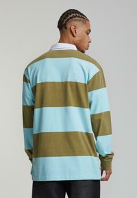 Ilgi piedurkņu polo krekls ar maiņošām gaiši zila un olīvu zaļa svītrām, baltu apkakli un mīkstu auduma struktūru.