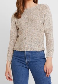 Dziany sweter z okrągłym dekoltem, wielokolorowymi drobinkami, długimi rękawami i ściągaczem na dole, zestawiony z wysokim stanem niebieskich jeansów.