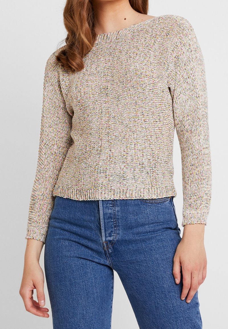 Dziany sweter z okrągłym dekoltem, wielokolorowymi drobinkami, długimi rękawami i ściągaczem na dole, zestawiony z wysokim stanem niebieskich jeansów.