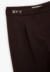 Donkerbruine broek met een strakke vormgeving, plooien en een goudkleurige sluitingdetails bij de taille. Gladde stof met een subtiele glans.