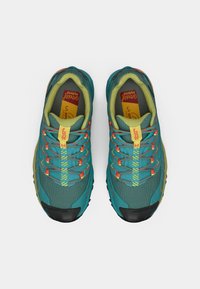 Ténis de corrida turquesa e amarelo com pormenores laranja. Apresenta um cabedal em malha, tecido texturizado e uma sola de borracha com cravos multidireccionais.
