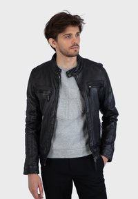 Čierna kožená bunda s stojacím golierom, so zipsovými prsiakovými vreckami a hladkou textúrou, nosená na sivej mikine.