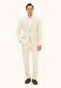 Lichtbeige linnen pak met een enkele rij knopen en twee zakken, gecombineerd met bijpassende broek en bruine instapschoenen.