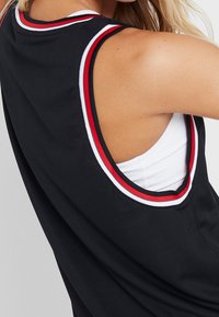 Maillot de sport noir avec une texture en maille, présentant des accents rayés rouges et blancs sur l'encolure et les emmanchures.