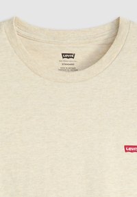 Beige Levi's Rundhals-T-Shirt mit rotem Logoaufnäher auf der Brust und aufgedruckten Markendetails im Kragen.
