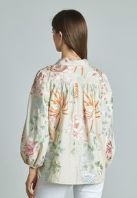 Blusa ricamata realizzata in un tessuto leggero e testurizzato, caratterizzata da motivi floreali nei toni di rosa, arancione, verde e blu, con maniche a palloncino.