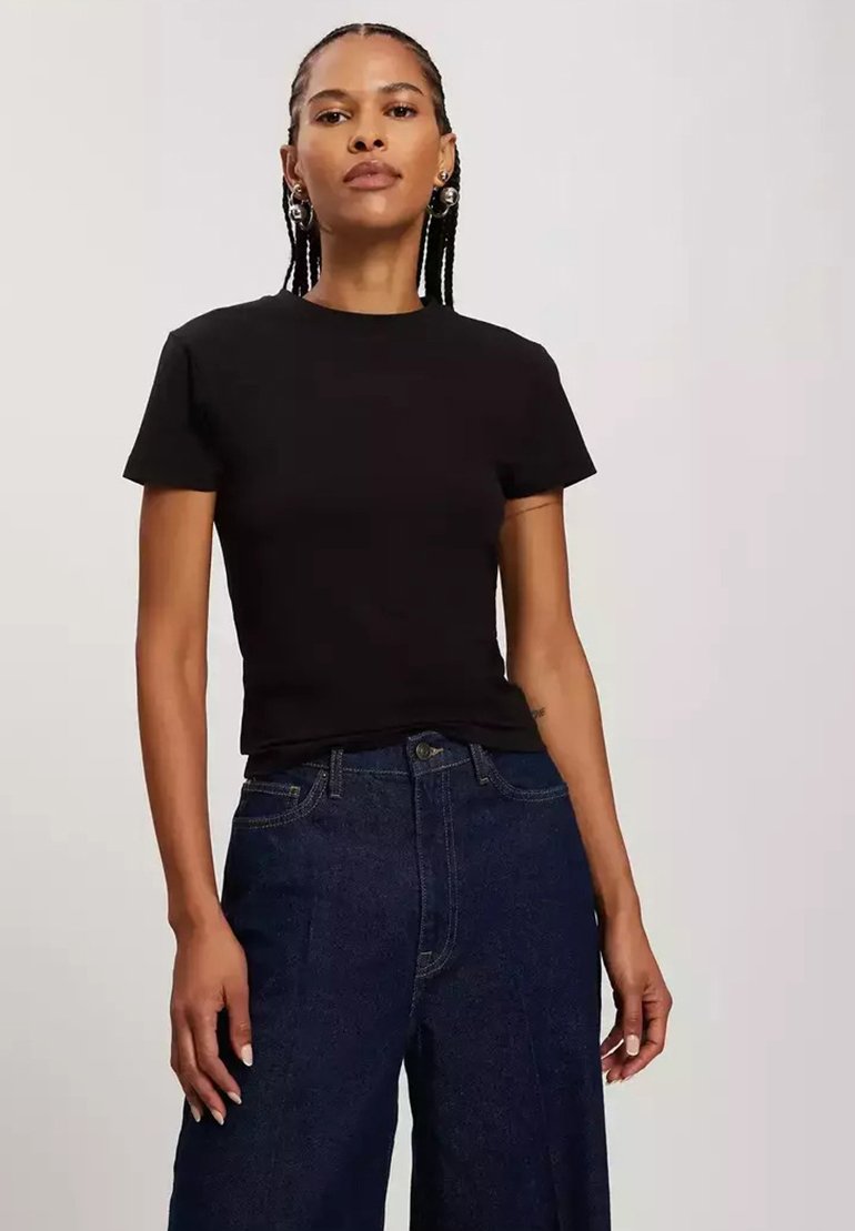 Czarna koszulka z krótkim rękawem, wykonana z bawełny, z klasycznym okrągłym dekoltem. Noszona z ciemnoniebieskimi spodniami typu wide-leg z wysokim stanem.