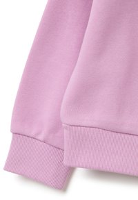Tela de sudadera en rosa claro con puños acanalados, textura suave y un ajuste holgado, destacando las costuras en la muñeca y el cuerpo.