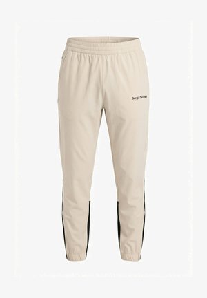 Pantaloni da allenamento beige Sergio Tacchini con vita elasticizzata, strisce laterali nere, caviglie con zip e logo sulla coscia sinistra superiore.