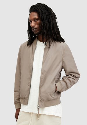 Chaqueta bomber en color taupe claro con una textura suave. Presenta puños y dobladillo acanalados, cierre frontal de cremallera y bolsillos laterales para mayor funcionalidad.