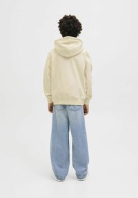 Beigais kapucis ar aukliņu, ar brīvu piegriezumu un ribotām piedurknēm, apvienots ar platiem gaiši zilajiem džinsiem.