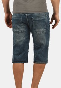 Shorts cargo en denim bleu foncé, avec un design longueur genou, deux poches arrière avec des coutures contrastantes et une texture décolorée.