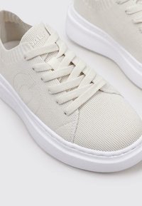 Zapatillas blancas ligeras con una parte superior de malla texturizada, cordones planos y una suela de goma suave con sutiles acentos de logo.
