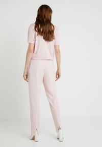 Light pink short-sleeve top paired with light pink trousers featuring side slits. White block-heeled shoes complete the outfit. Simple, clean design.