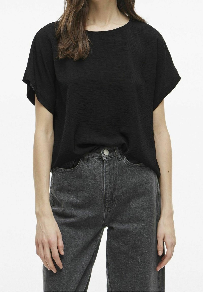 T-shirt noir texturé avec un col rond et des manches courtes, associé à un jean en denim gris foncé taille haute. Design simple, coupe décontractée.