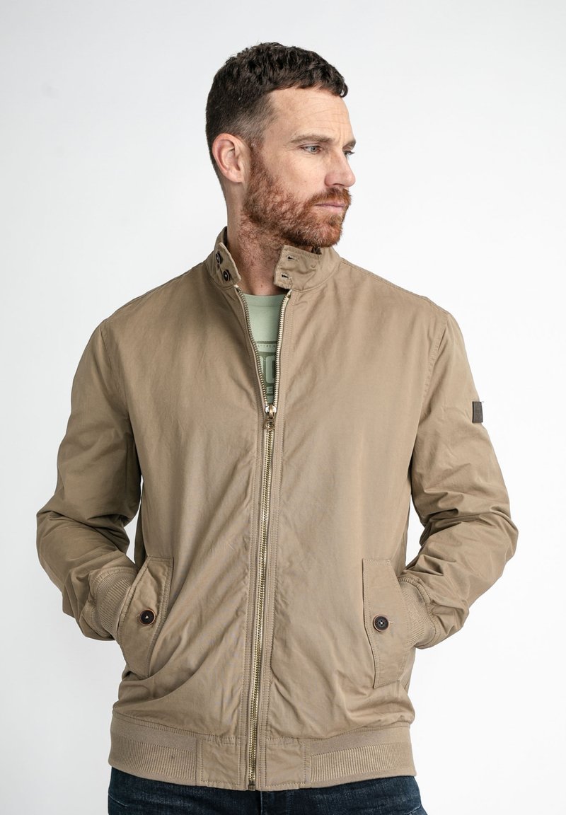 Chaqueta bomber marrón claro con cuello alto, cremallera frontal, dos bolsillos laterales, puños acanalados y una tela suave, ligeramente texturizada.