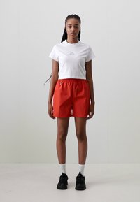 White cropped t-shirt, red elastic shorts, black sneakers, white socks. Simple, functional design with no visible patterns or graphics.
