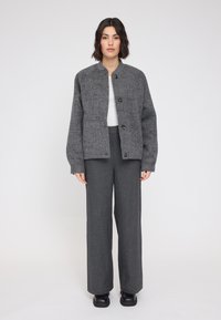Gray wool jacket with a round collar and three front buttons, paired with gray wide-leg pants and black shoes. Textured fabric and relaxed fit.