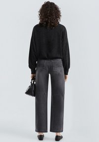 Oversized zwarte trui met een subtiele glans, gecombineerd met hooggetailleerde, grijze wijde jeans met achterzakken en een rechte pasvorm.